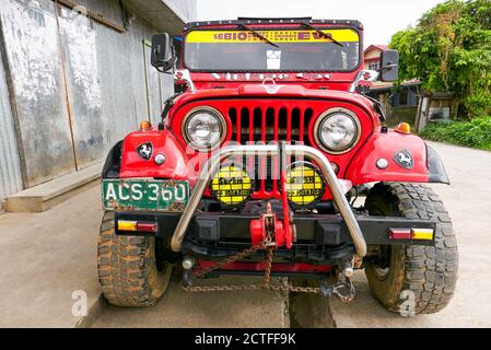 Vue rapprochée d'une voiture tout-terrain de style jeep de couleur rouge à 4 roues motrices avec de très grandes roues, pare-chocs et phares, vue à Sagada, Philippines Banque D'Images