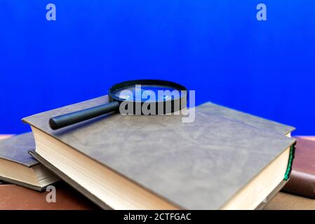 Mise au point sélective loupe quelques livres fermés sur un table en bois marron fond bleu Banque D'Images