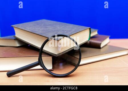 Mise au point sélective loupe quelques livres fermés sur un table en bois marron fond bleu Banque D'Images