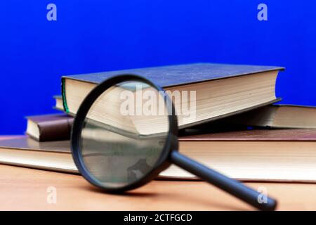 Mise au point sélective loupe quelques livres fermés sur un table en bois marron fond bleu Banque D'Images