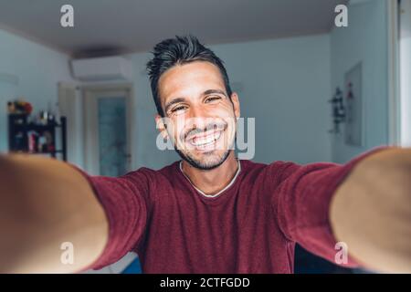 Un jeune homme charmant et heureux qui prend un selfie à la maison - Un homme positif souriant à l'intérieur de l'appareil photo Banque D'Images