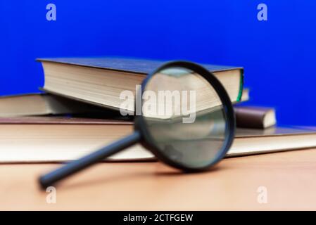 Mise au point sélective loupe quelques livres fermés sur un table en bois marron fond bleu Banque D'Images