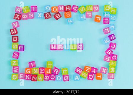 Perles cubes en plastique multicolore avec lettres éparpillées sur fond bleu et mots Bonjour. Texture d'arrière-plan alphabétique anglais Banque D'Images