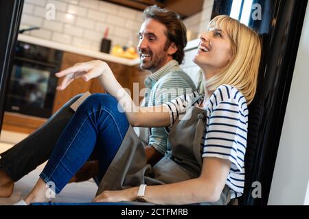 Les jeunes professionnels fatigué couple sitting on plancher de la cuisine après la cuisson Banque D'Images