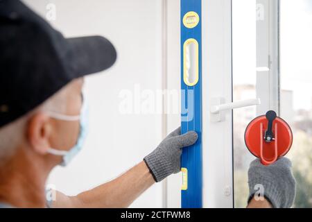 L'homme de travail dans le masque médical installe les fenêtres en plastique upvc et portes blanches avec ventouse de levage Banque D'Images