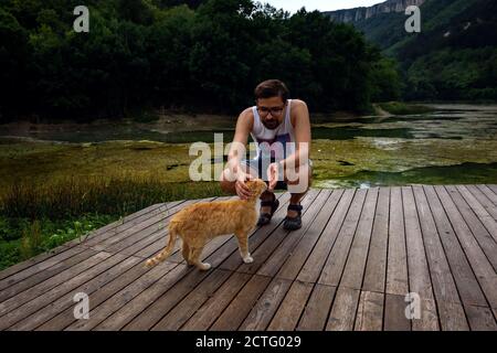 Un homme joue avec un chat tabby rouge domestique. Le chat frotte sur la jambe de l'homme. Après la pluie Banque D'Images
