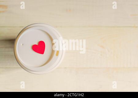 tasse à café jetable en papier artisanal et coeur en bois rouge sur un chapeau. On peut aller sur une table en bois Banque D'Images