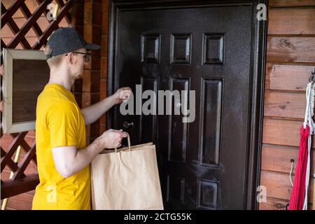 jeune liveur tenant des sacs en papier de nourriture tout en frappant sur la porte de la maison Banque D'Images