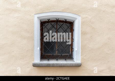 Vieux mur de bâtiment biège avec une petite fenêtre vintage avec une grille métallique rouillée de fer. Détail de la façade dans une ville européenne âgée Banque D'Images