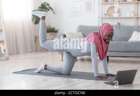 Femme islamique noire sportive dans le hijab Excersising à la maison avec Ordinateur portable Banque D'Images