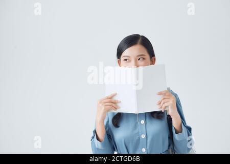 Joyeuse fille sombre-cheveux couvre son visage avec son carnet blanc Banque D'Images