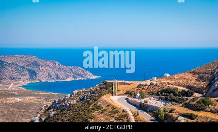 Vue panoramique du cimetière du village de Menetes et du mémorial de guerre, avec la baie de Pigadia en arrière-plan, île de Karpathos, Grèce Banque D'Images