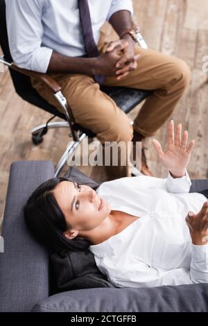 vue du dessus du patient en train de parler et de gesturer pendant qu'il est allongé canapé près d'un psychologue afro-américain Banque D'Images