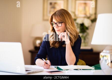 Femme d'affaires confiante et mûre assise au bureau et travaillant sur un ordinateur portable. Bureau à domicile. Banque D'Images