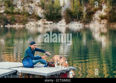 Homme chien propriétaire et ami beagle chien sur la jetée en bois sur le lac de montagne et appréciant le paysage pendant leur marche en automne saison. Banque D'Images