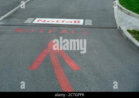 Deux panneaux sur la rue ou la route asphaltée écrits en allemand et tous deux signifiant la salle d'urgence, ER, avec une grande flèche rouge. Banque D'Images