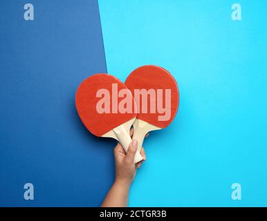 la main femelle tient deux raquettes de ping-pong en bois sur fond bleu, gros plan Banque D'Images