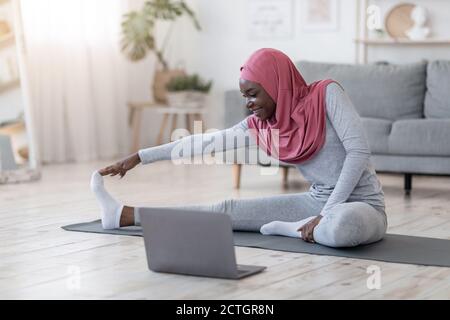 Formation à domicile. Femme musulmane noire sportive s'étendant devant un ordinateur portable Banque D'Images