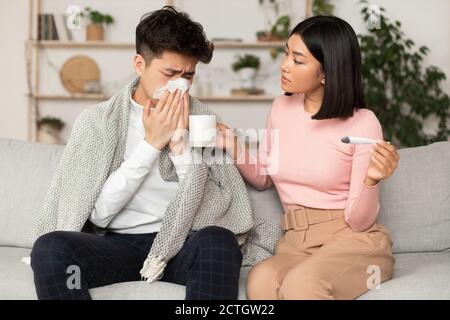 Femme chinoise traitant mari malade donnant des médicaments assis à la maison Banque D'Images