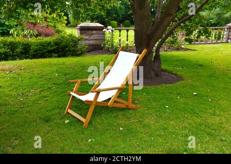 Une chaise longue blanche vide, à l'ancienne, à l'extérieur dans le jardin anglais, sur une pelouse en herbe par un arbre à l'ombre du soleil d'été Banque D'Images