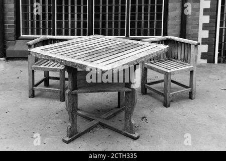 Image en noir et blanc de la table en bois rustique isolée et chaises à l'extérieur du bâtiment sur un patio en béton en été Banque D'Images