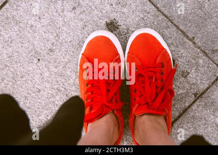 Pieds femelles vus d'en haut. Selfie pour toute utilisation. Pied et jambes en baskets rouges. Pied debout sur les carreaux gris. Avec espace de copie. Pieds à l'extérieur près de u Banque D'Images