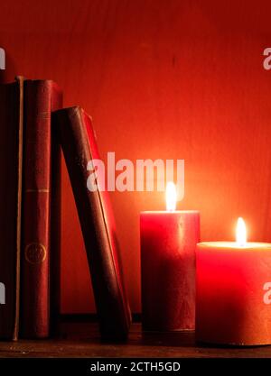 Vieux livres et bougies éclairées sur une table en bois, fond rouge aux chandelles, vertical Banque D'Images