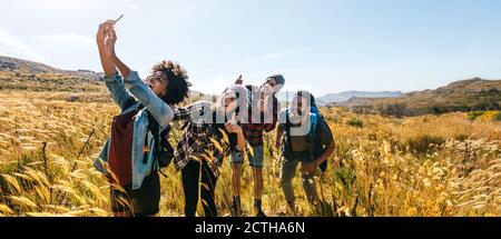 Des amis qui prennent le selfie sur la promenade à pied. Groupe d'hommes et de femmes qui font de la randonnée dans la campagne et prennent le selfie avec un téléphone. Banque D'Images