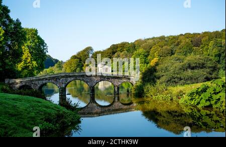 Le pont Palladien, un pont en pierre de cinq arches au-dessus de l'eau plate du lac avec des arbres qui commencent à montrer leurs feuilles d'automne dans les jardins de Stourhead. Banque D'Images