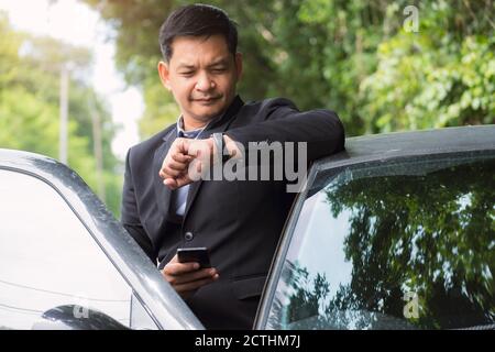 Portrait d'homme d'affaires portant un costume et regardant le temps debout près de sa voiture Banque D'Images