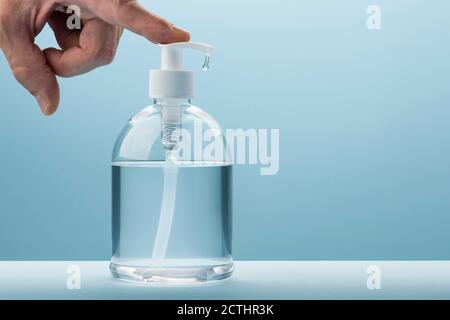 Main de l'homme pompe le gel antibactérien du distributeur sur fond bleu Banque D'Images