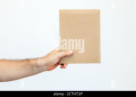 La main de l'homme tient une enveloppe en papier. Livraison de documents par service de messagerie. Livraison rapide express. Colis postal, paquet Banque D'Images