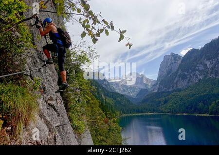 Jeune femme grimpant sur via Ferrata Laserer alpin Klettersteig à lac Goosausee sous la montagne de Dachstein Banque D'Images