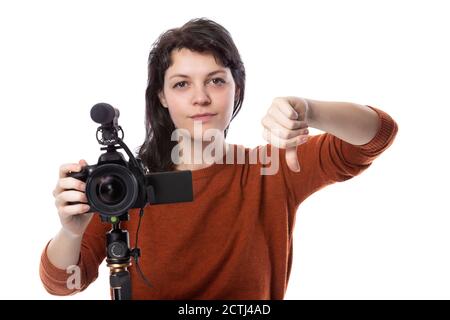 Jeune femme avec un appareil photo et un micro en tant que cinéaste ou créateur de contenu en ligne faisant un geste de pouce vers le bas. Elle ressemble à une étudiante en cinéma ou à une freelance. Banque D'Images