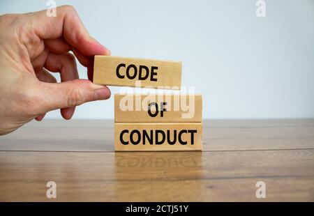 Main masculine plaçant un bloc avec le mot « code » au-dessus d'un bloc avec les mots « code de conduite ». Belle table en bois, fond blanc. Copier l'espace. Busi Banque D'Images