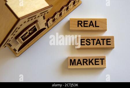 Des blocs en bois forment les mots « marché immobilier » près de la maison miniature. Arrière-plan blanc. Concept d'entreprise, espace de copie. Banque D'Images