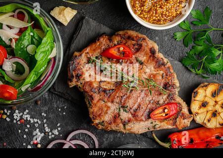 Steak de porc grillé avec légumes et salade fraîche sur fond sombre. Flat lay, vue de dessus. Banque D'Images