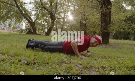 Homme sportif âgé effectuant des exercices de poussée. Entraînement cardio à l'extérieur dans le parc de la ville le matin. Portrait de la forme physique grand-père ancien appréciant le sport et un style de vie sain. Personnes âgées actives Banque D'Images