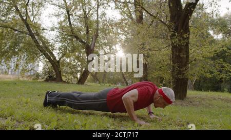 Senior actif âgé de 80 ans caucasien faisant des exercices physiques de poussée matinale dans le parc de la ville. Entraînement grand-père entraînement fitness. Un mode de vie sain à la vieillesse Banque D'Images