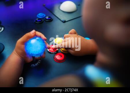 Un jeune garçon jouant à des jeux vidéo sur une salle d'arcade avec des boutons-poussoirs disposés dans un style de chasseur. Banque D'Images