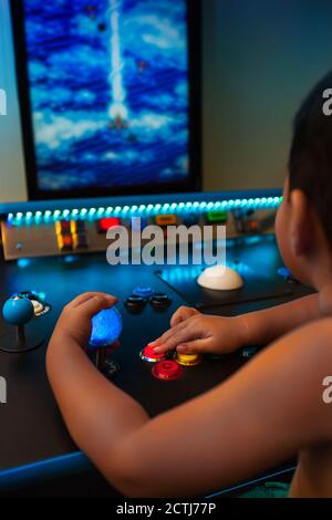 Gamin de quatre ans jouant à des jeux rétro sur une salle de jeux avec joystick lumineux et boutons sur un moniteur vertical. Banque D'Images