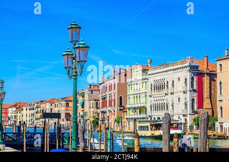 Quai avec poteaux en bois de la voie navigable du Grand Canal dans le centre historique de Venise avec rangée de bâtiments colorés architecture vénitienne, mouettes dans le ciel bleu. Vénétie, Nord de l'Italie. Banque D'Images