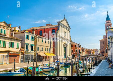 Chioggia paysage urbain avec canal d'eau étroit Vena avec des bateaux multicolores amarrés, église Chiesa dei Filippini, tour du Parrocchia di San Giacomo Apostolo bâtiment et pont en briques, Italie du Nord Banque D'Images