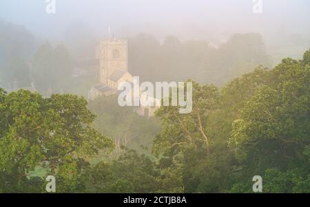 L'église Saint-Wilfrid de Burnsall devient visible lorsque le soleil levant brûle l'épais brouillard qui entoure le joli village des Yorkshire Dales. Banque D'Images