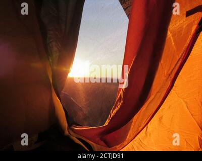 Orange camping touristique tente fenêtre donnant sur le soleil au lever du soleil. Loisirs dans la nature romantique Banque D'Images