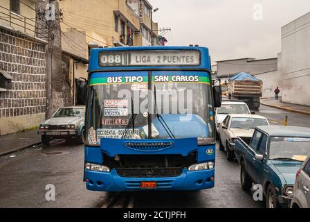 Quito, Equateur - 2 décembre 2008 : gros plan frontal d'un bus public privé bleu coincé dans la circulation des voitures et des camions sous la pluie. Appartements jaunes Banque D'Images