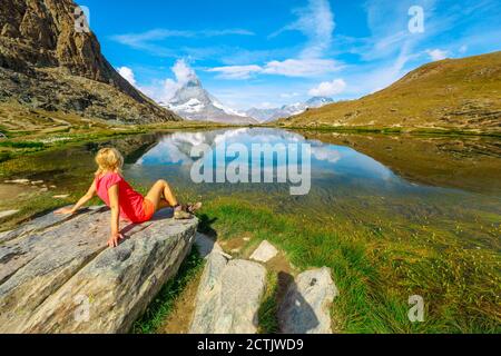Le mont Cervin se reflète sur le lac Riffelsee. Femme de tourisme se détendant après une randonnée depuis la gare de Rotenboden sur le chemin de fer à crémaillère de Gornergrat. Tourisme à Banque D'Images