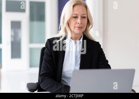 Femme d'affaires confiante travaillant sur un ordinateur portable tout en étant assise à la maison Banque D'Images