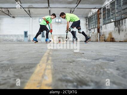 Vue au niveau de la surface du père et du fils face à face en jouant au roller hockey sur le terrain Banque D'Images