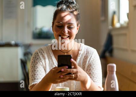 Gros plan d'une femme voluptueuse souriante utilisant un téléphone portable lorsqu'elle est assise dans le restaurant Banque D'Images